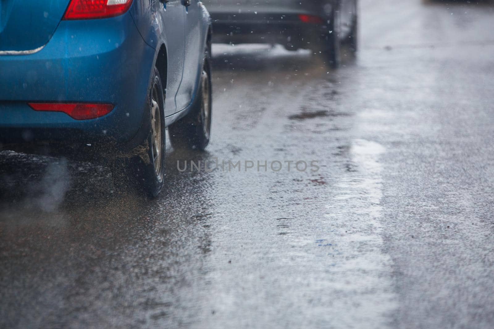 Dirt water splash flow from wheels of blue car moving fast in daylight city with selective focus. Car moving on dirty asphalt road after spring snow melting.