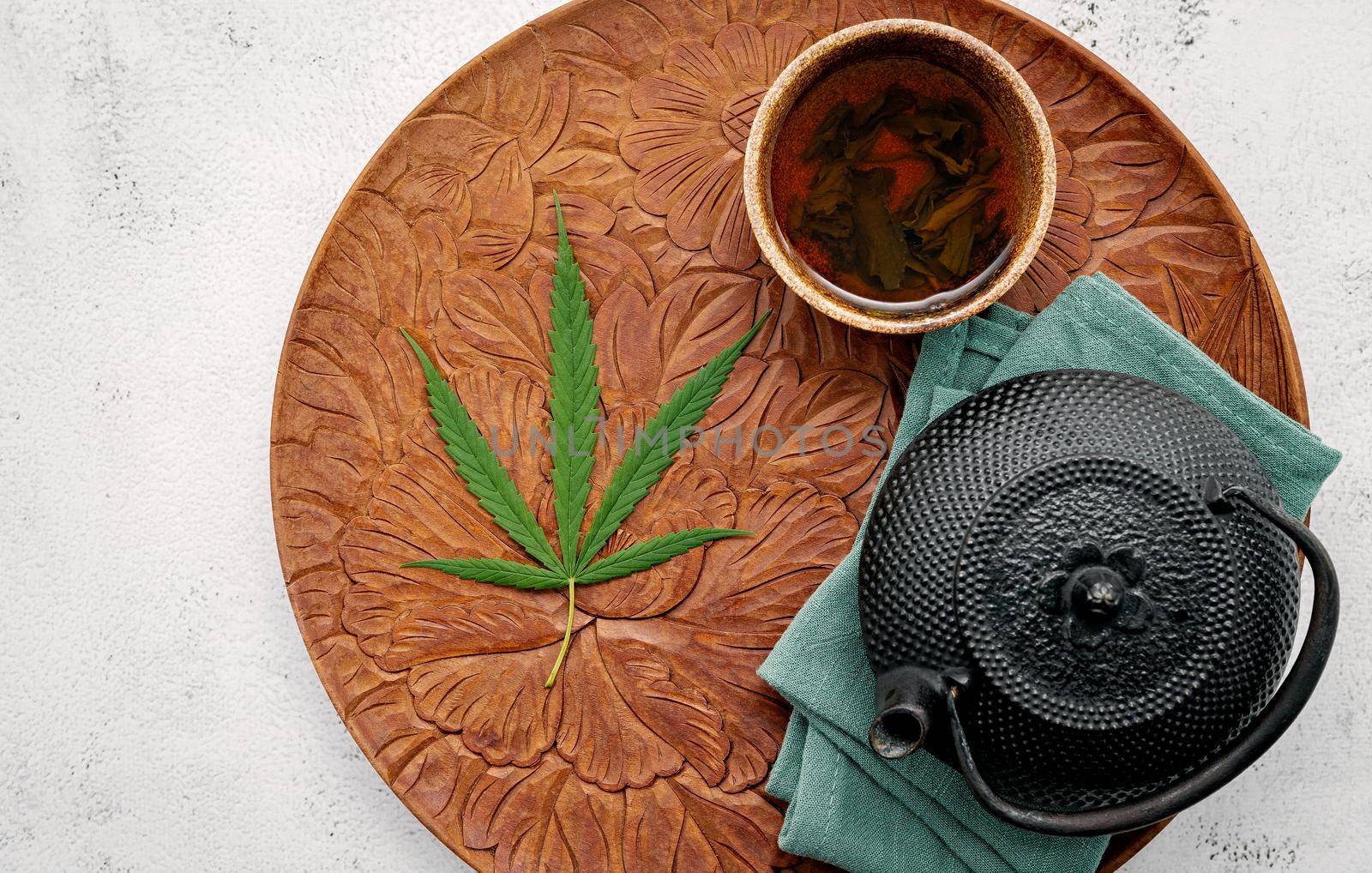 Vintage teapot with cannabis herbal tea and fresh marijuana leaves set up on concrete background. by kerdkanno