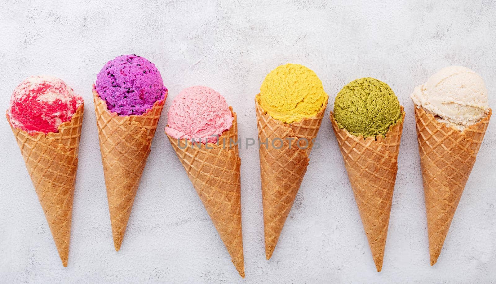 Various of ice cream flavor in cones blueberry ,pistachio ,almond ,orange and cherry setup on white stone background . Summer and Sweet menu concept.  by kerdkanno
