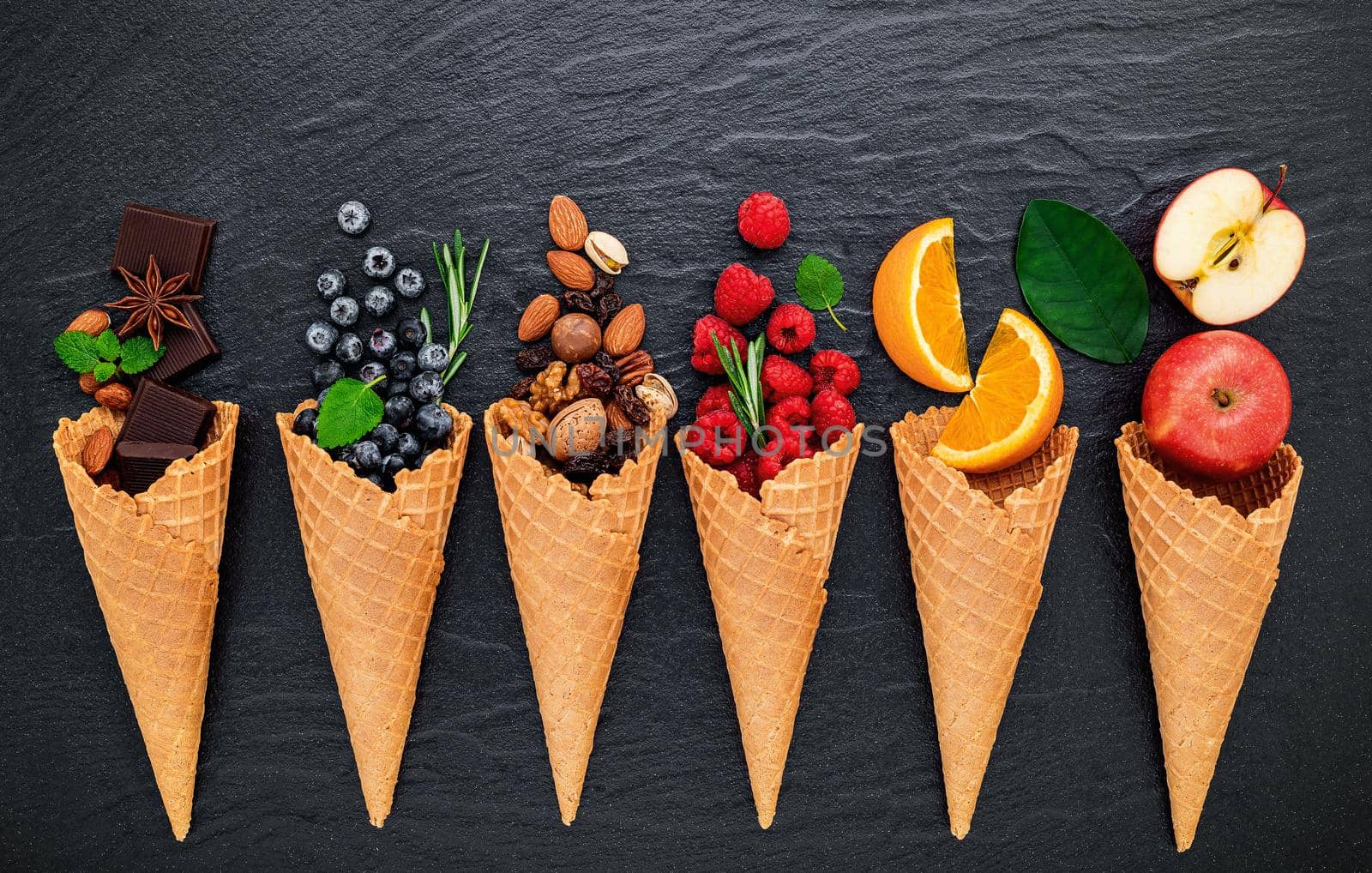 Various of ingredient for ice cream flavor in cones blueberry ,lime ,pistachio ,almond ,orange ,chocolate ,vanilla and coffee set up on dark stone background . Summer and Sweet menu concept. by kerdkanno