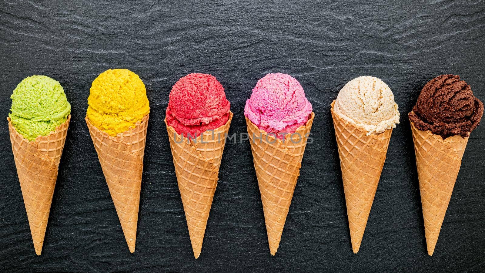 Various of ice cream flavor in cones blueberry ,lime ,pistachio ,almond ,orange ,chocolate ,vanilla and coffee set up on dark stone background . Summer and Sweet menu concept. by kerdkanno