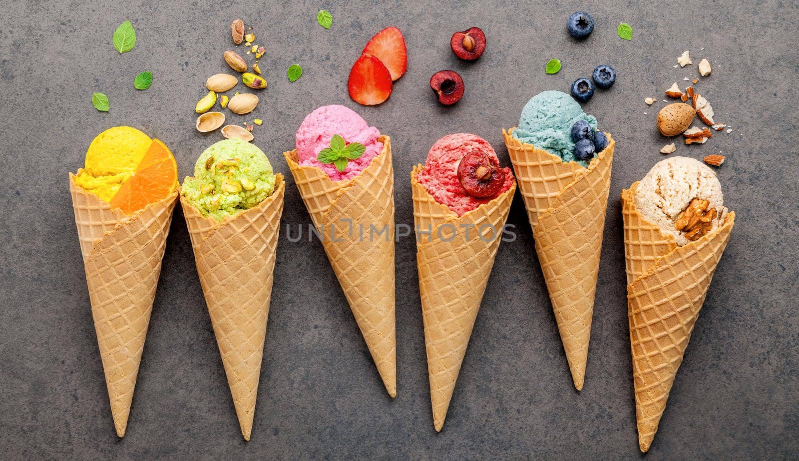 Various of ice cream flavor in cones blueberry ,strawberry ,pistachio ,almond ,orange and cherry setup on dark stone background . Summer and Sweet menu concept. by kerdkanno