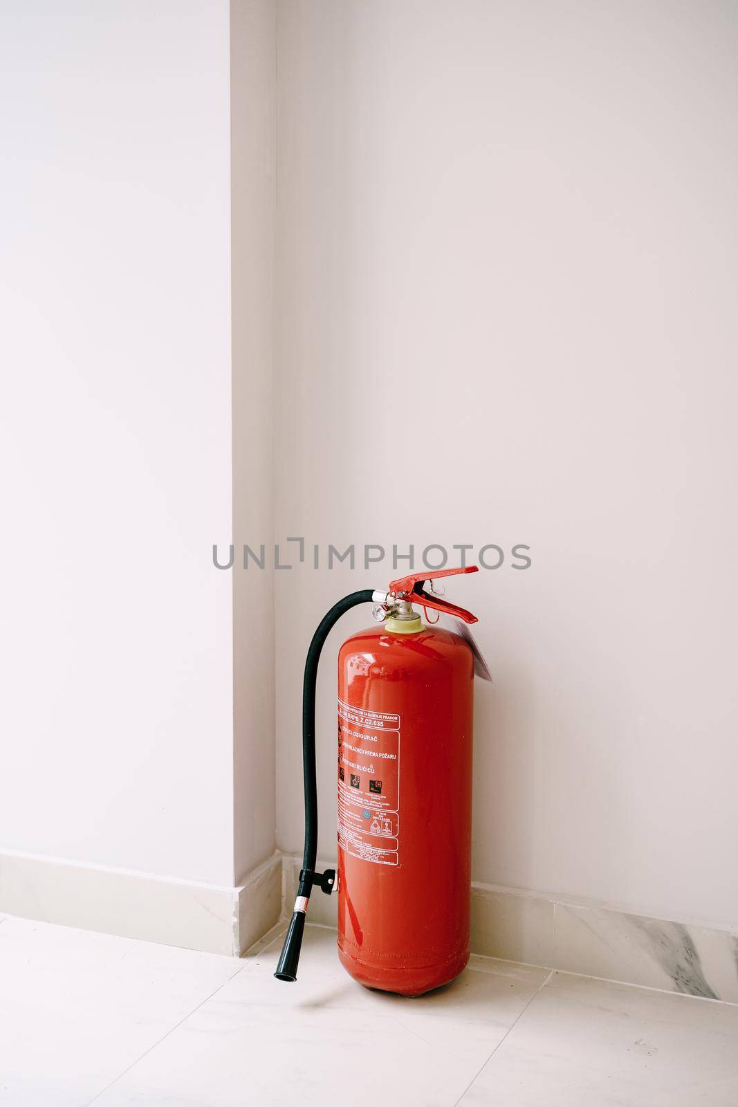 A red fire extinguisher on the floor in the corner against a white wall. High quality photo