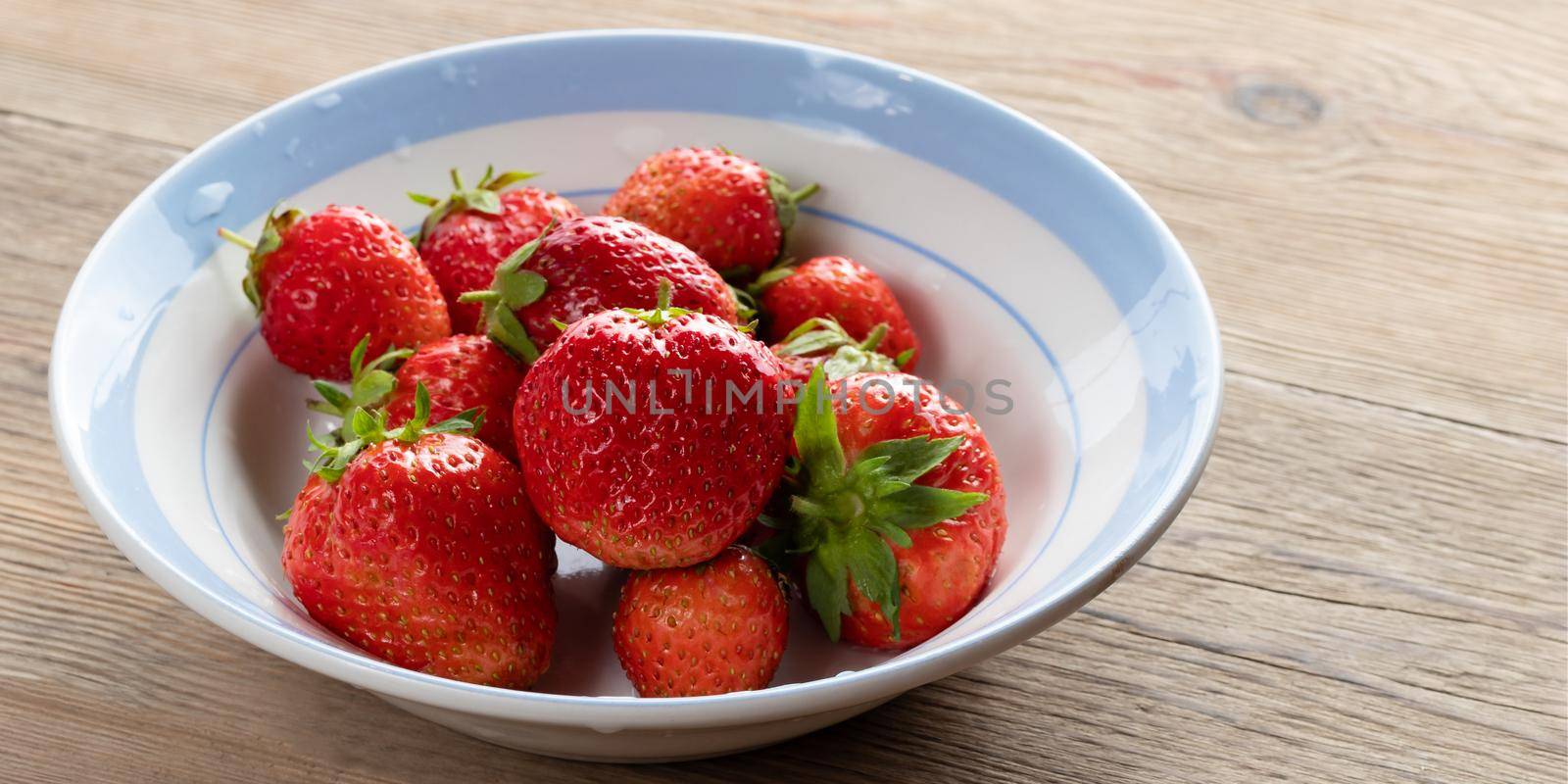Natural ripe strawberries in a plain white bowl on a wooden table.
