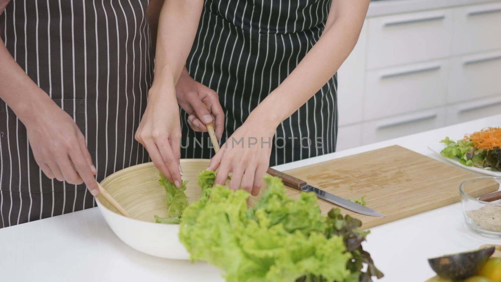 Happy Asian beautiful family couple husband and wife cooking vegetable salad in kitchen together at home. The man mix the vegetables in a cup woman cut vegetables. healthy food concept