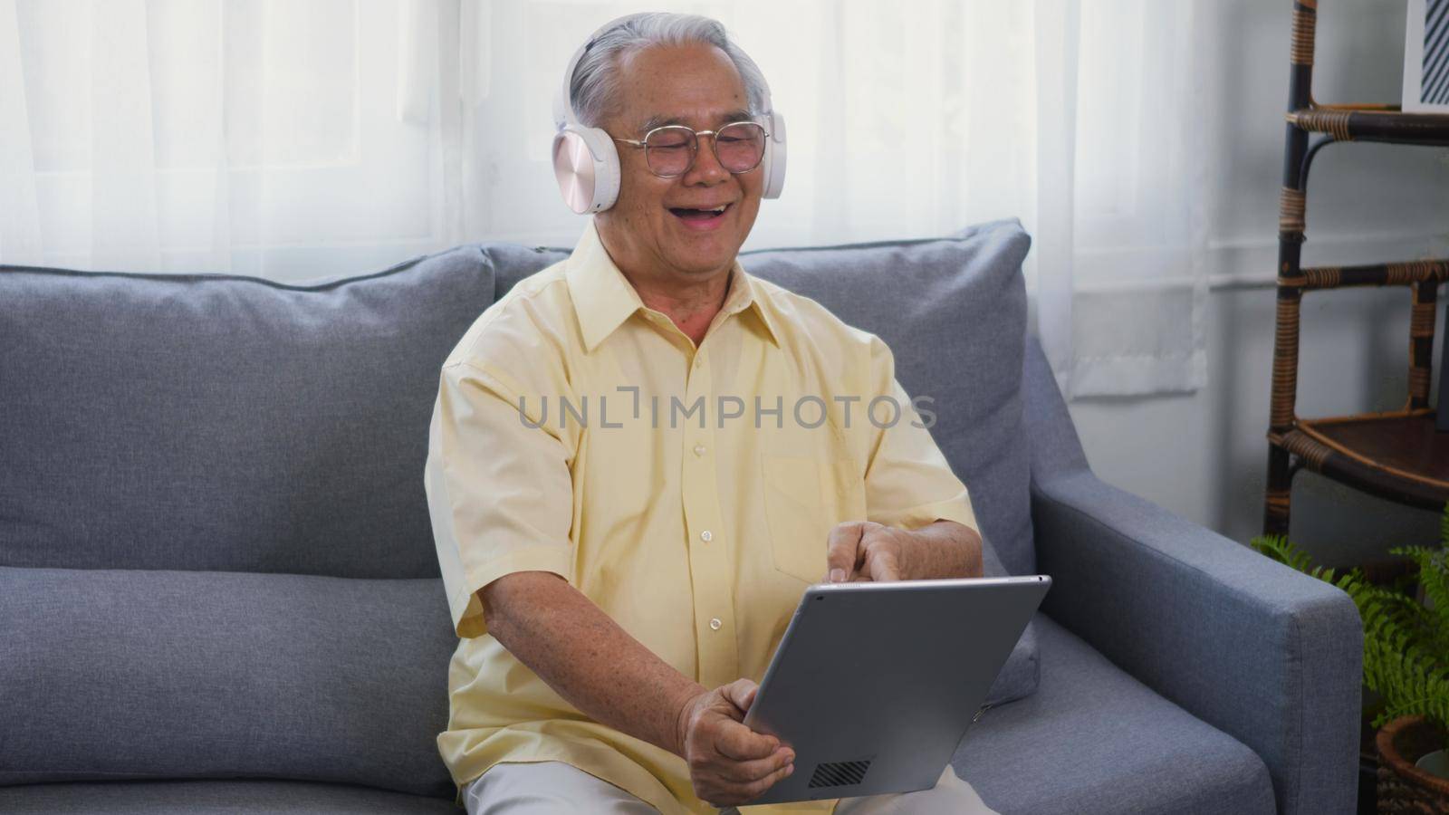 Old man grandfather smile relaxing wear headphones is listening to music using a digital tablet by Sorapop