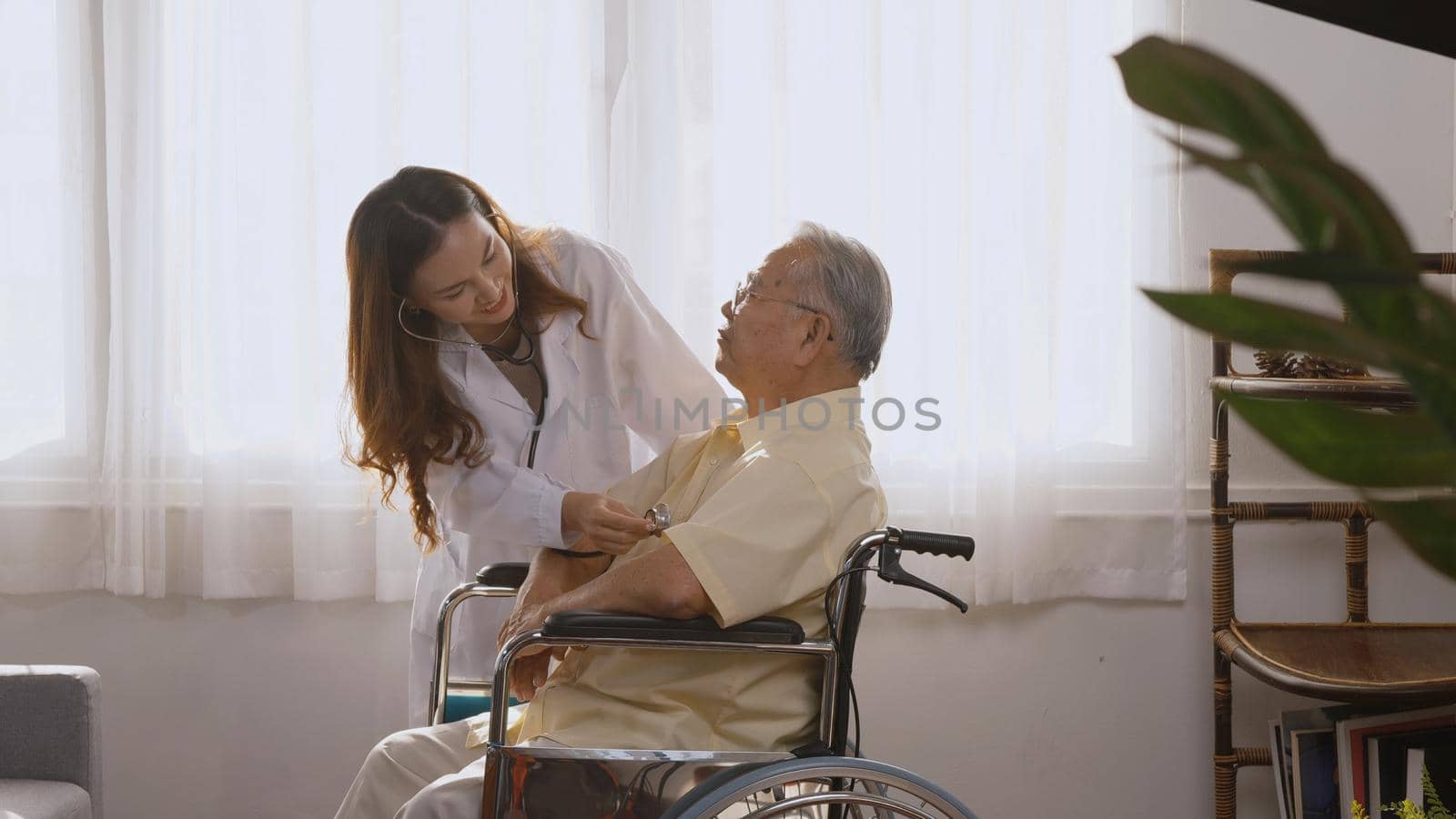 Female nurse doctor wear white uniform cardiologist examining patient senior or elderly old man during sit on wheelchair listening checking heartbeat using stethoscope at home, Health visitor concept