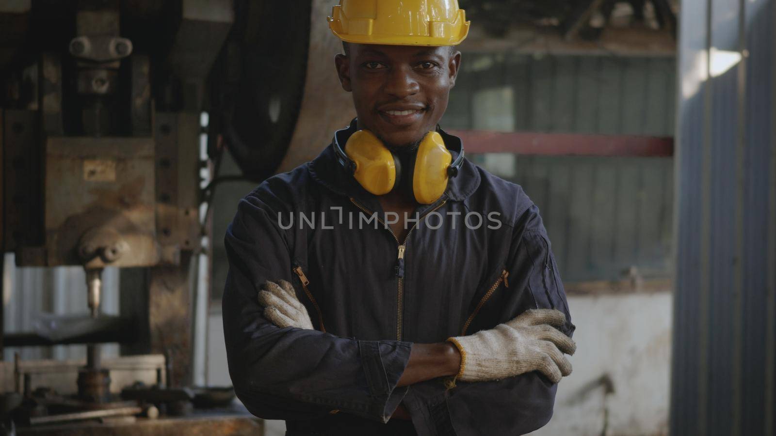 Portrait American industrial black young worker man smiling with yellow helmet in front of machine, Happy engineer standing arms crossed at work in the industry factory, manufacturing.