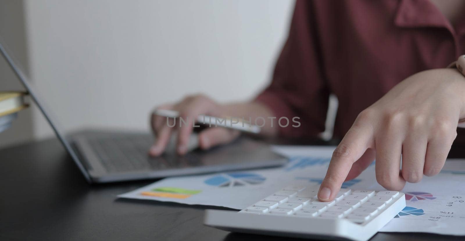 Close up Business woman using calculator and laptop for do math finance on wooden desk in office and business working background, tax, accounting, statistics and analytic research concept by wichayada