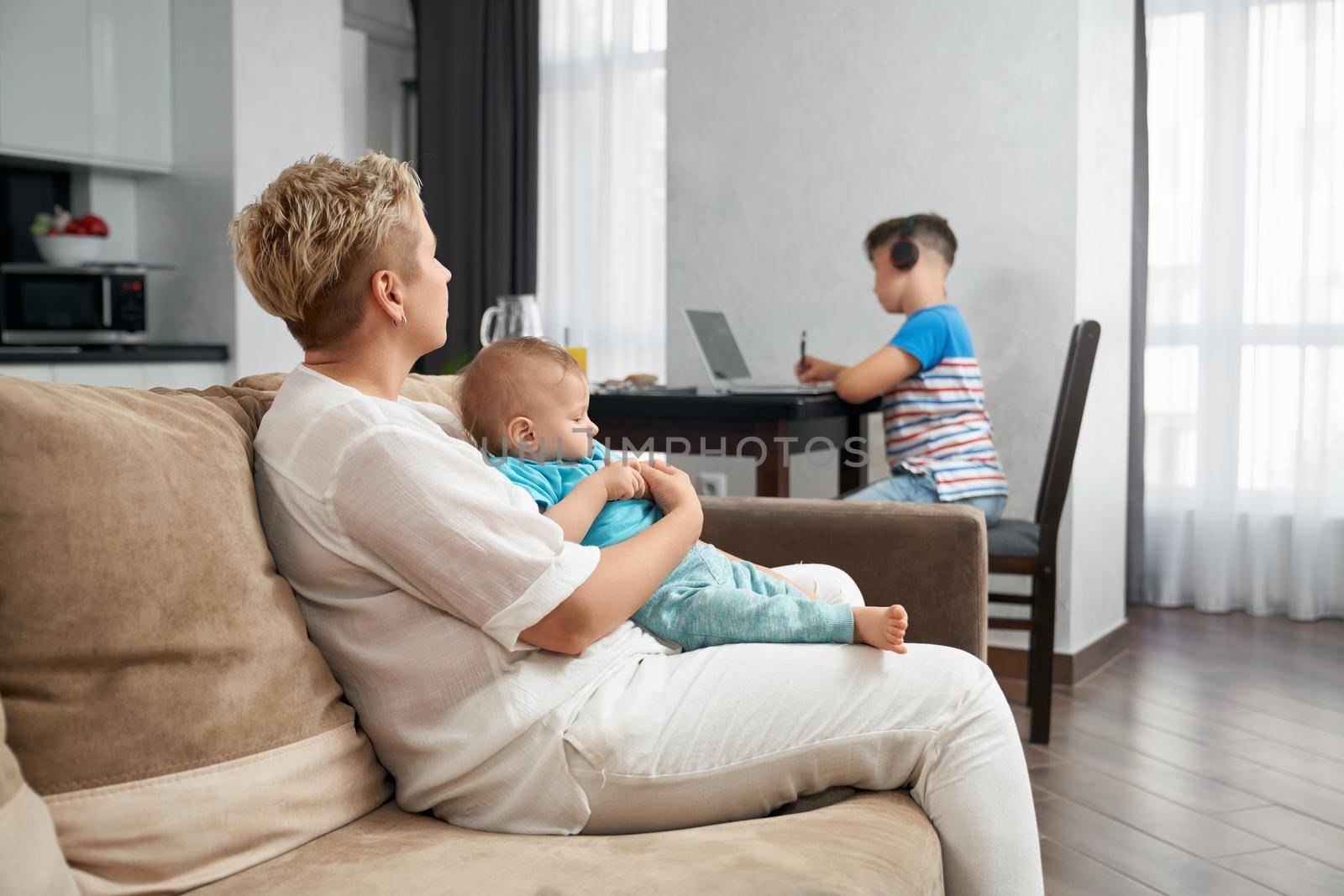 Woman playing with toddler while eldest son using laptop by SerhiiBobyk