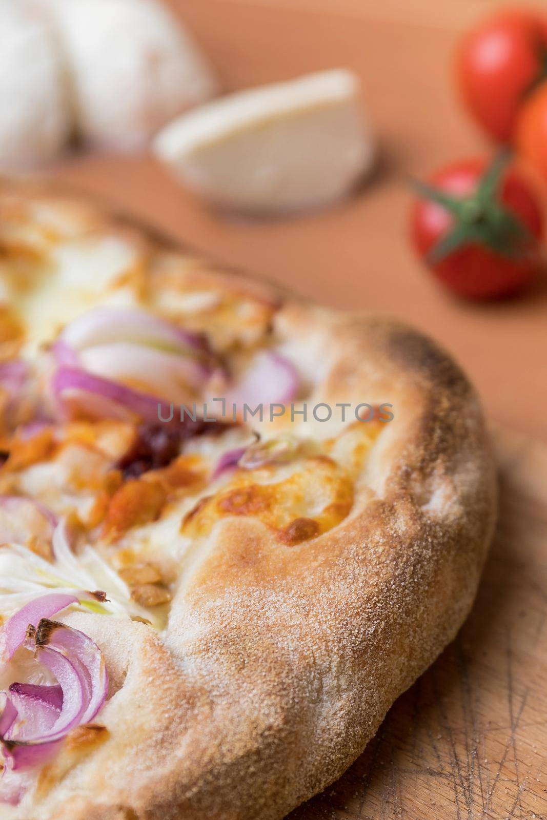 Pizza with cheese on a rustic wooden table. In the background out of focus cherry tomatoes and mozzarella.