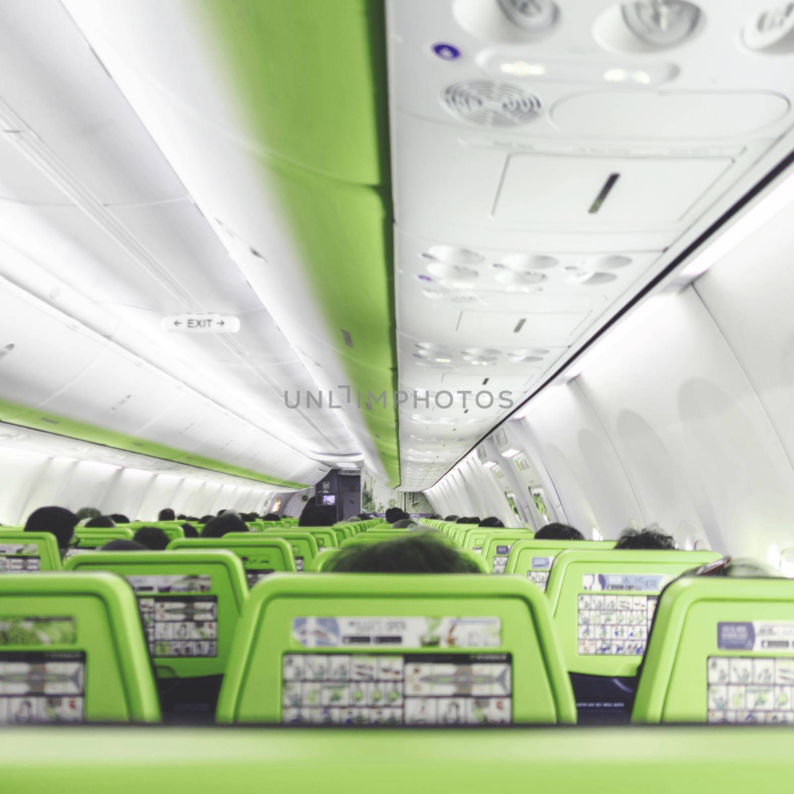 People on board the plane. Blurred foreground. Airplane interior with people sitting on green seats.