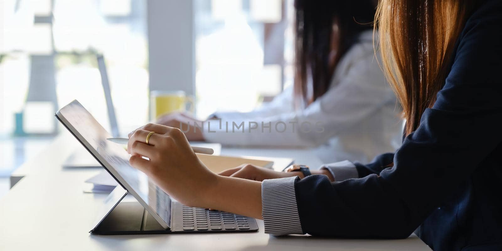 Young creative designer holding stylus and hand pointing at tablet while sitting at home office with her team. work from home concept
