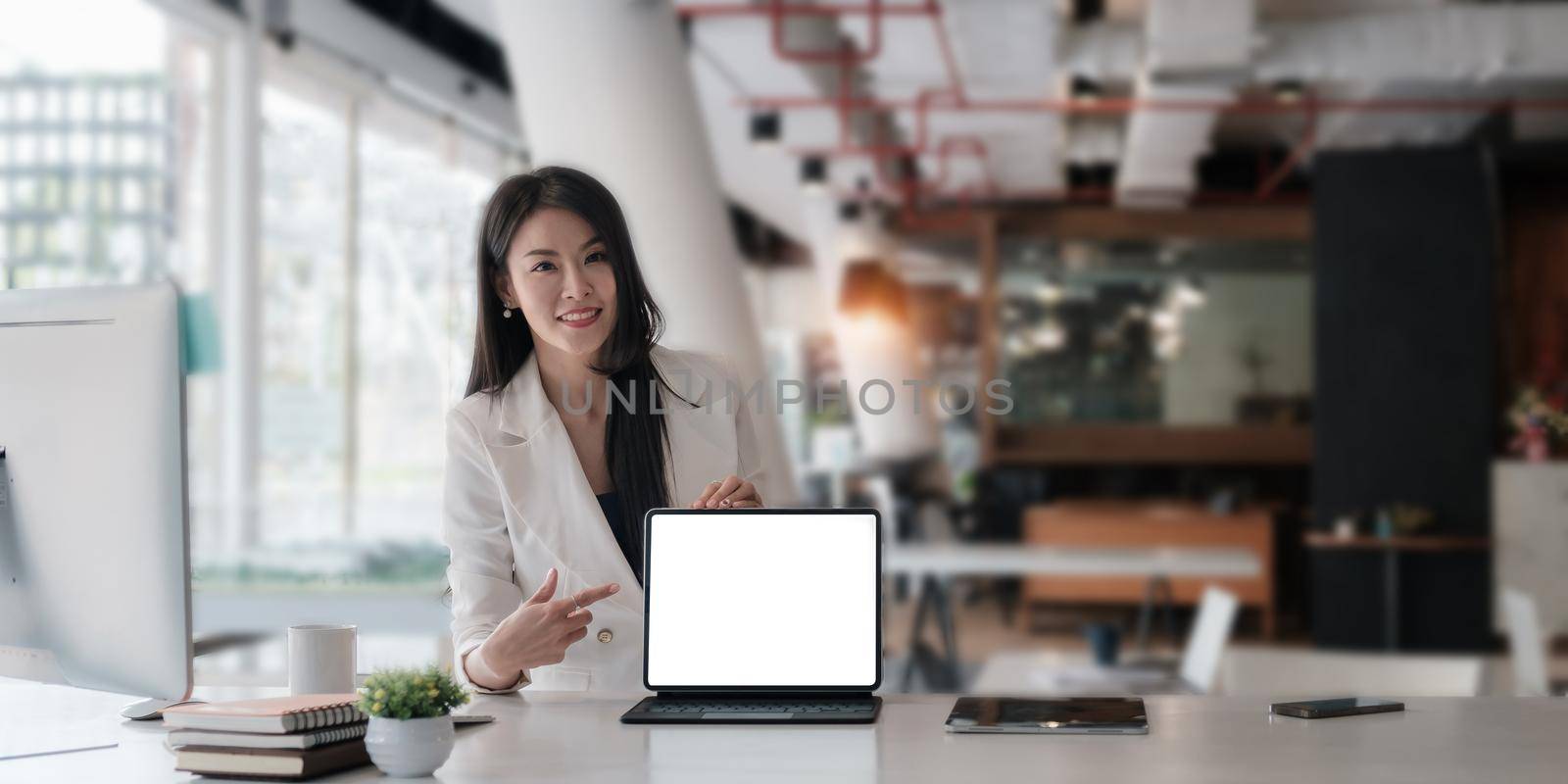 Business woman holding and pointing at digital tablet with blank screen in coffee shop.