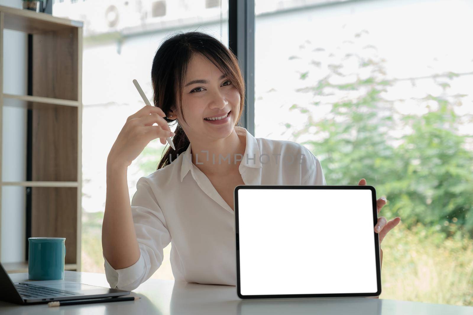 Business woman holding and pointing at digital tablet with blank screen in home office