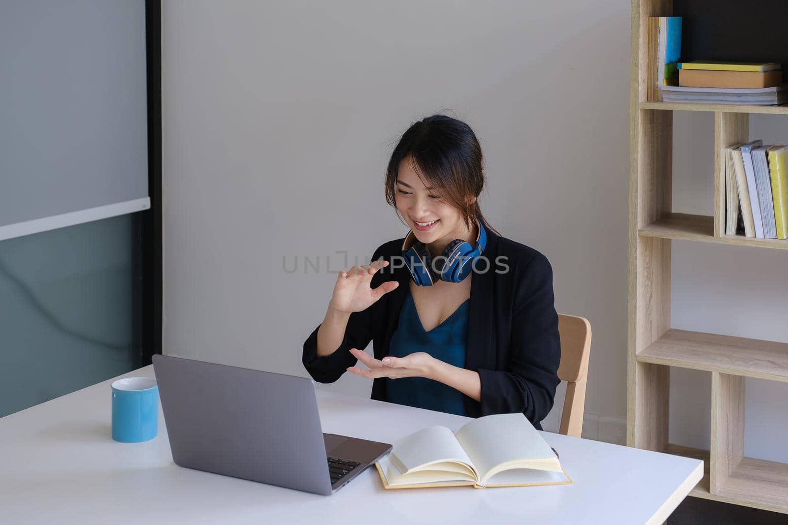 Happy young asian business woman with headphone to greeting or presentation to partner during making video conference with her team