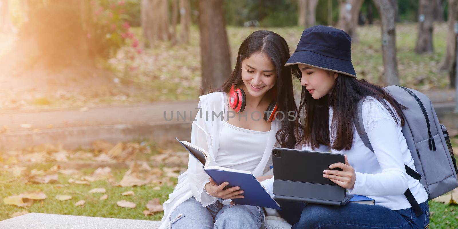 Two students are sitting in park during reading a book and communication. Study, education, university, college, graduate concept