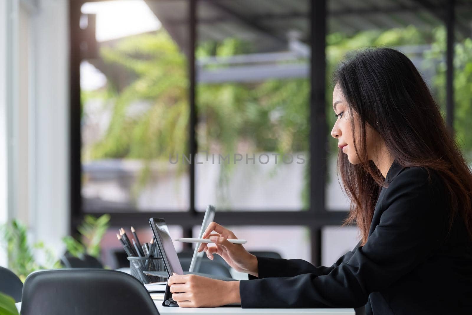 Young asian woman using digital tablet with pen stylus while sitting at her office desk in modern office by nateemee