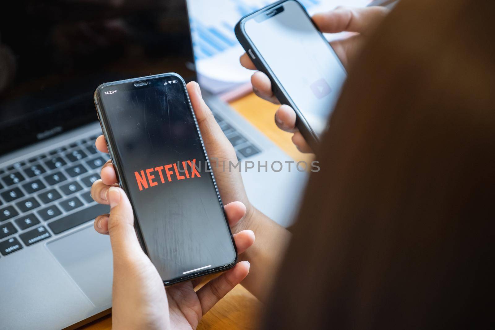 CHIANG MAI, THAILAND - FEB 11, 2021 : Woman and friend holding Phone with Netflix logotype on a screen and sharing her movie list