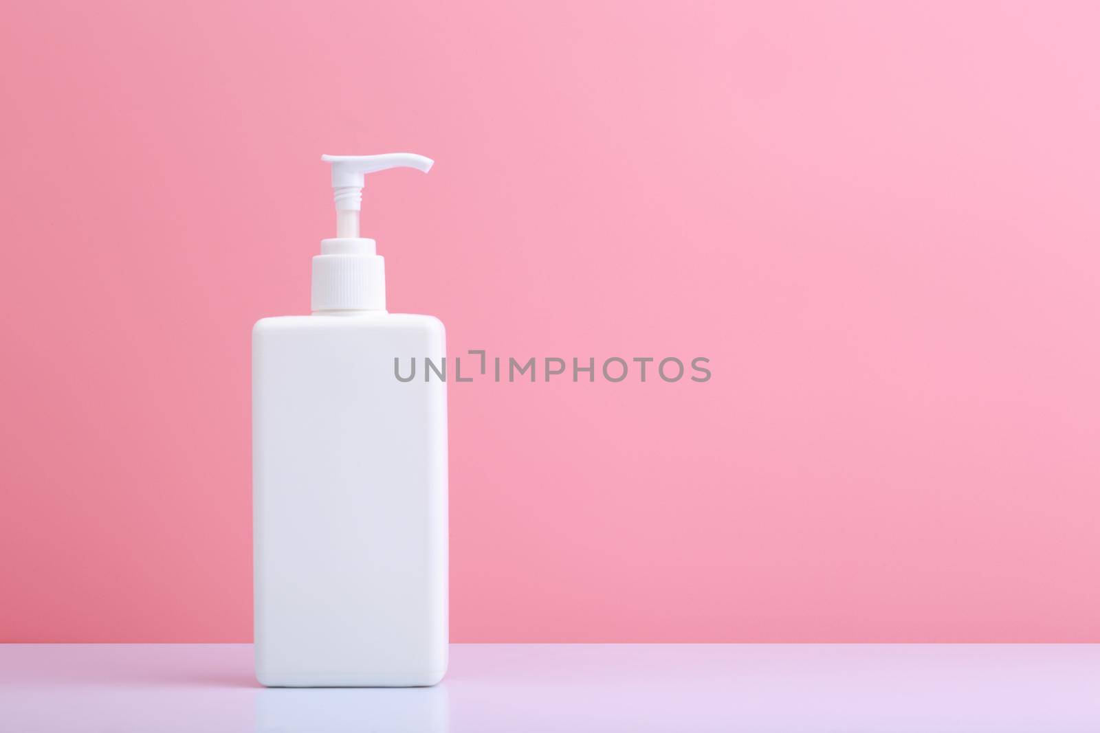 Body cream in tall white tube with dispenser against pink background with copy space by Senorina_Irina