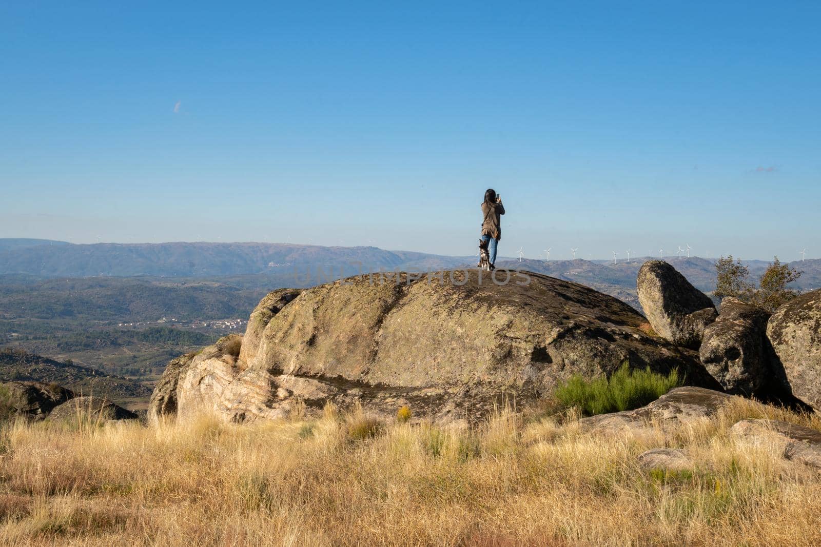 Caucasian young woman with brown dog on top of a boulder stone seeing Sortelha nature mountain landscape, in Portugal