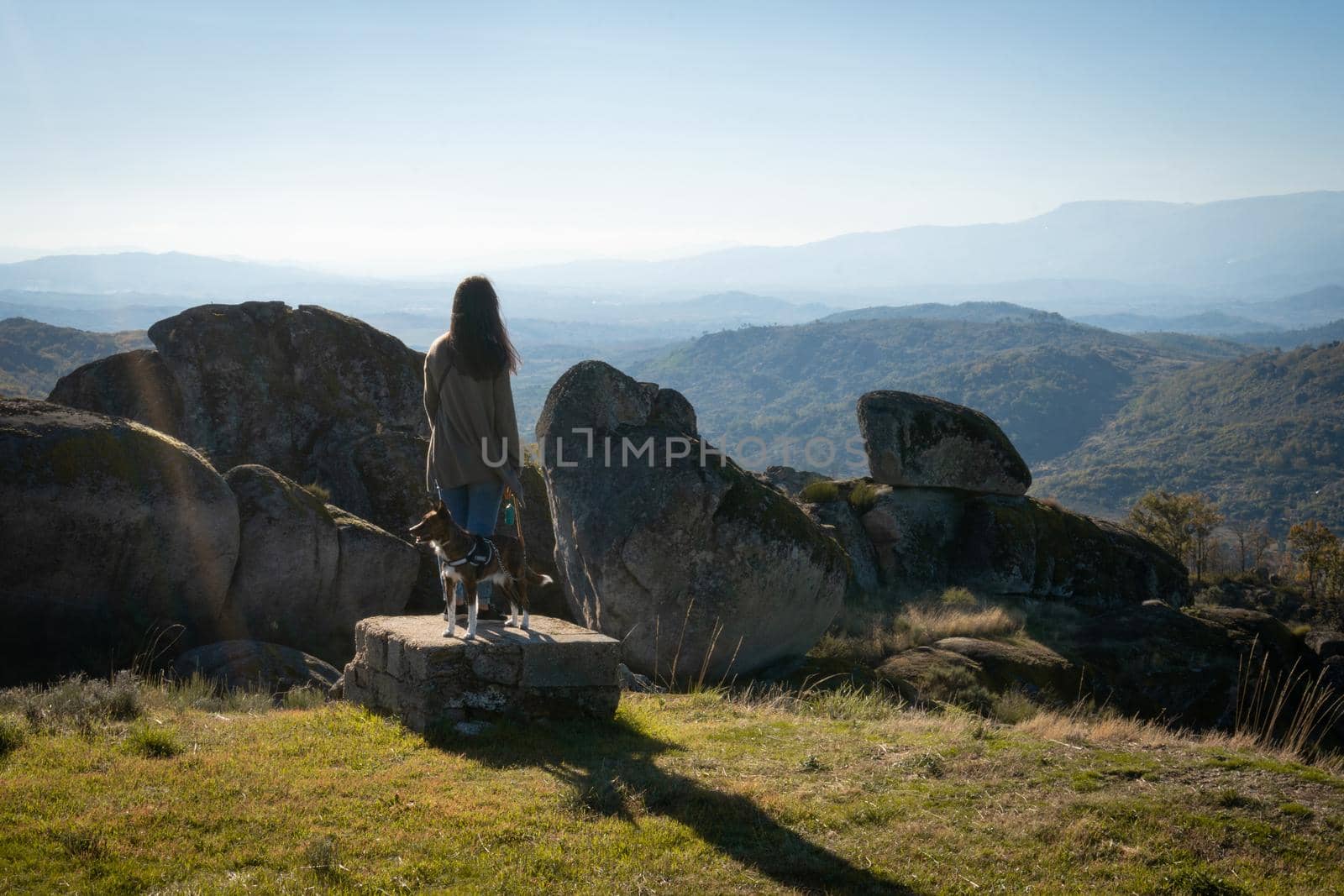 Caucasian young woman with brown dog on top of a boulder stone seeing Sortelha nature mountain landscape, in Portugal