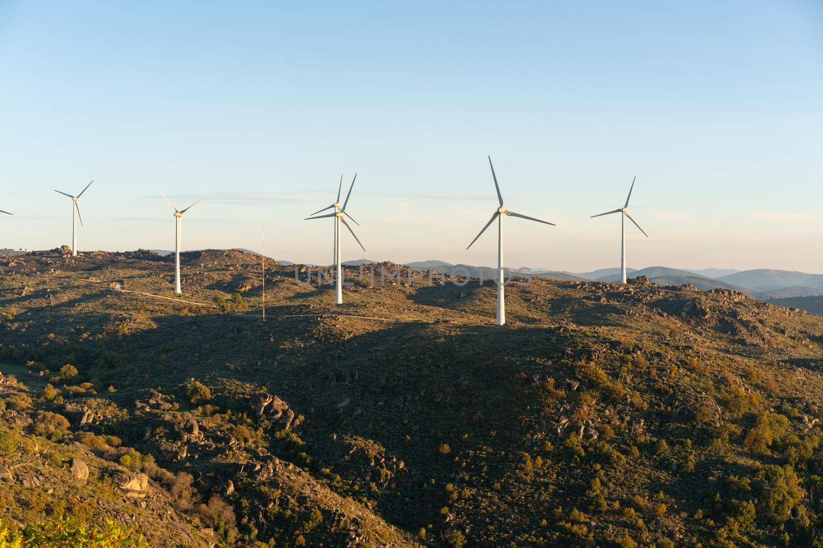 Sortelha nature landscape view with mountains, trees, boulders and wind turbines at sunset, in Portugal