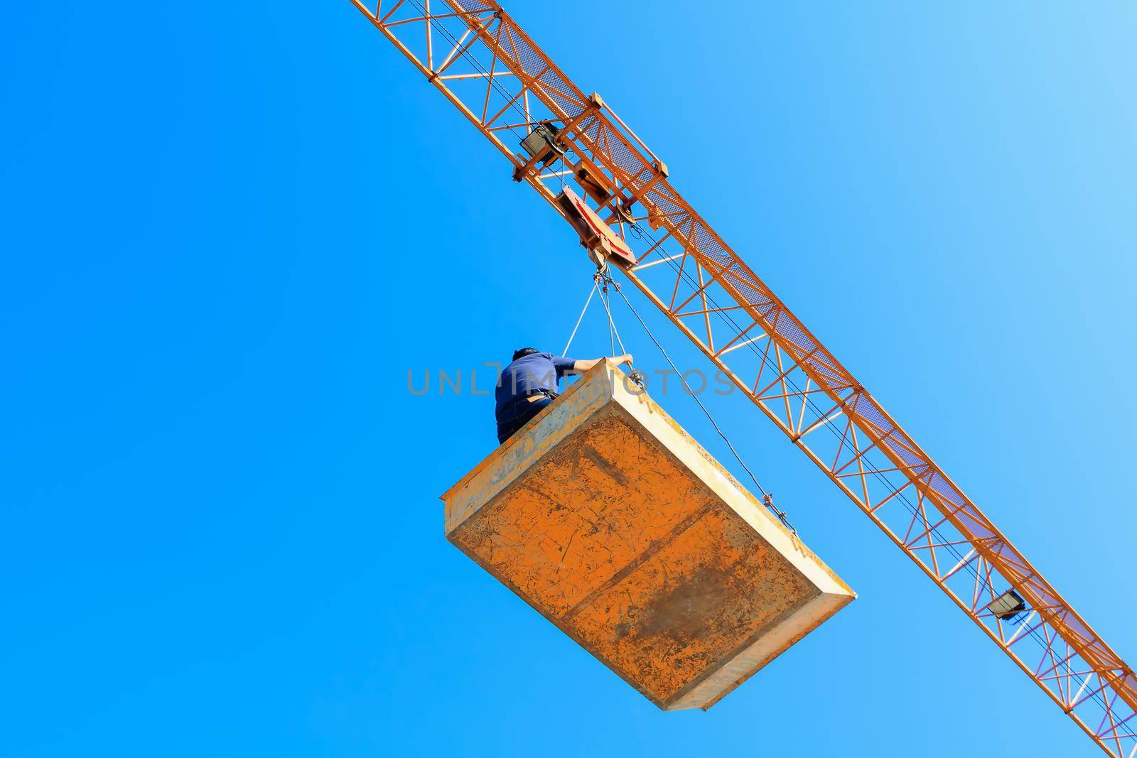 male in bucket of Tower crane. building construction site. blue sky background by pramot