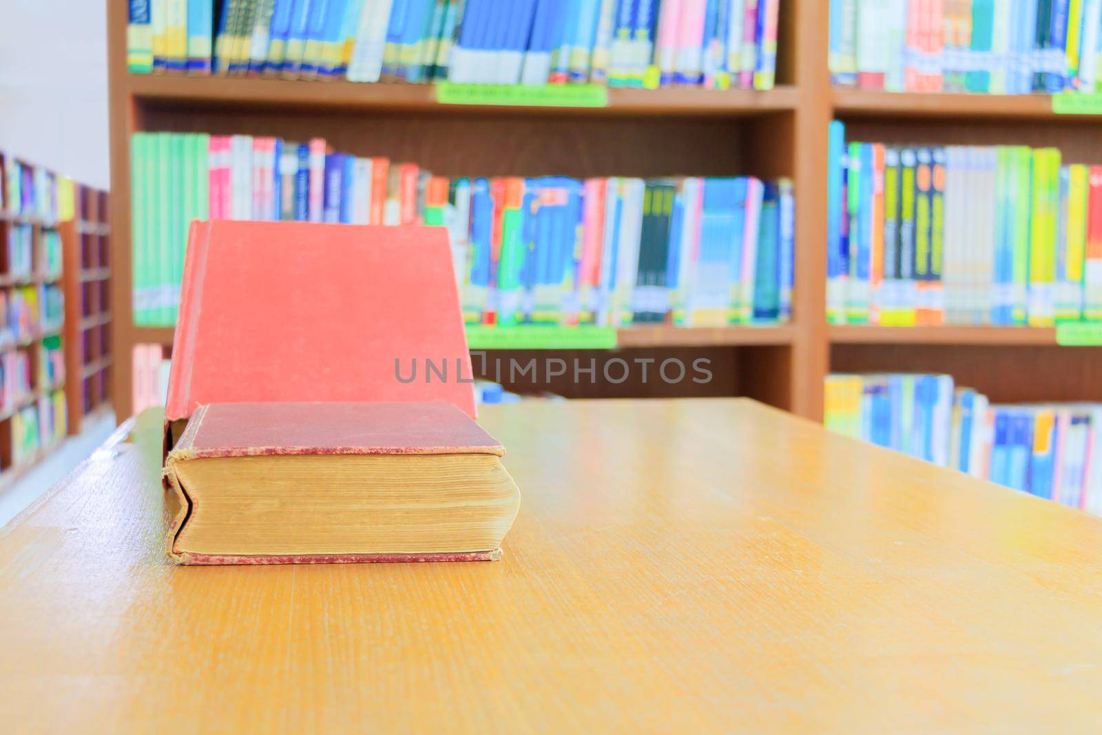 old book red and heap treatise in school library on wooden table. blurry bookshelves background. education learning concept with copy space add text