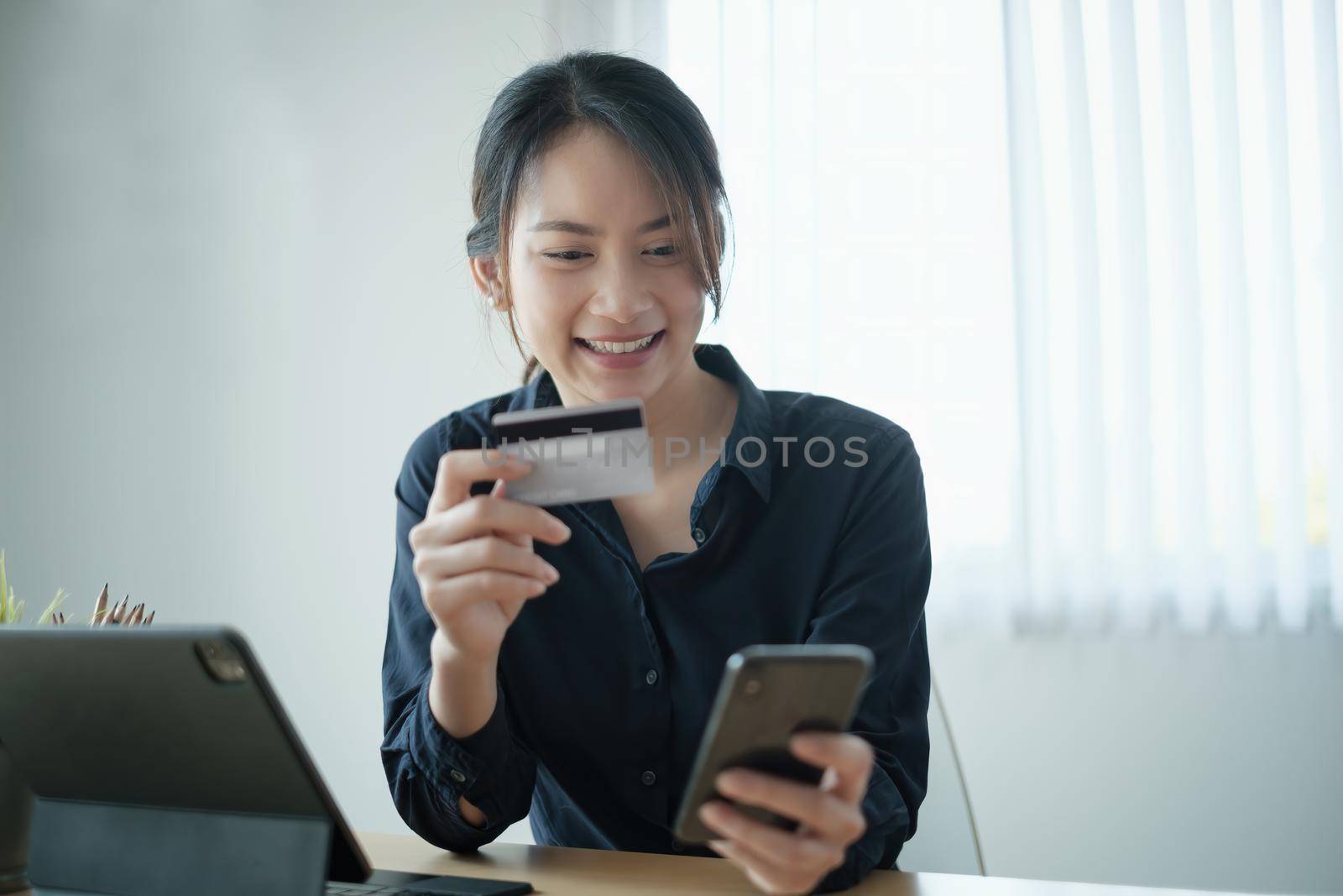 Woman in casual shirt paying with credit card online while making orders via application on cell phone. Successful and happy business woman making transaction using mobile bank application. by itchaznong