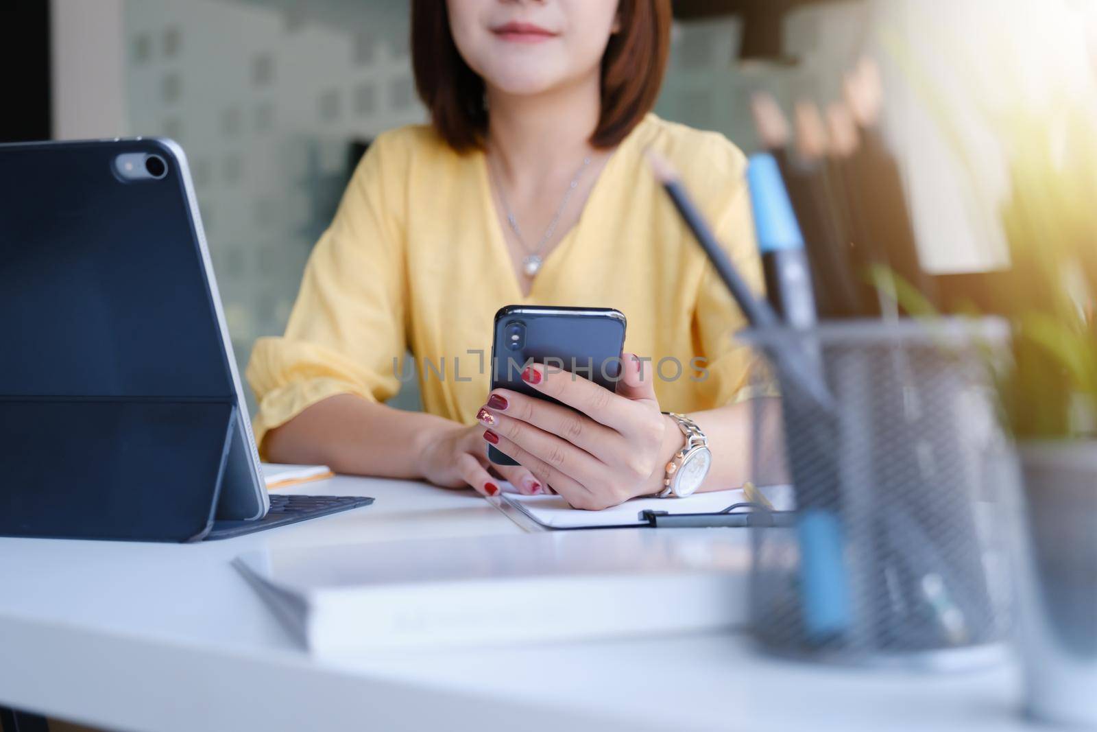 Young asian business woman using smart phone for contact customer on wooden desk in office. Business portrait concept. by itchaznong