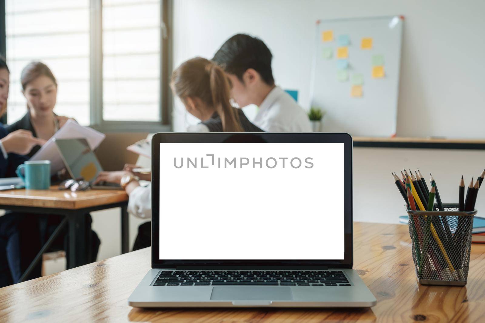 Laptop computer mockup and blank screen on wooden table with business team working background and morning light. by itchaznong