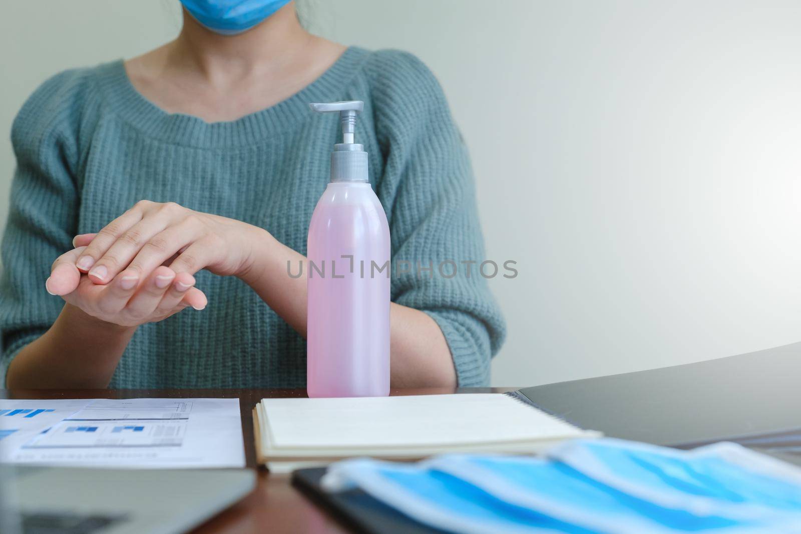 Businesswoman in mask washing hands by alcohol sanitizers or alcohol gel from pump bottle to kill corona virus or covid-19. work from home concept