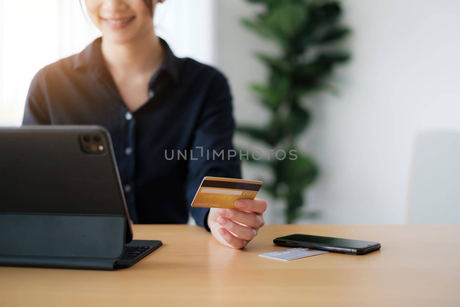 Woman in casual shirt paying with credit card online while making orders via application on tablet. Successful and happy business woman making transaction using mobile bank application
