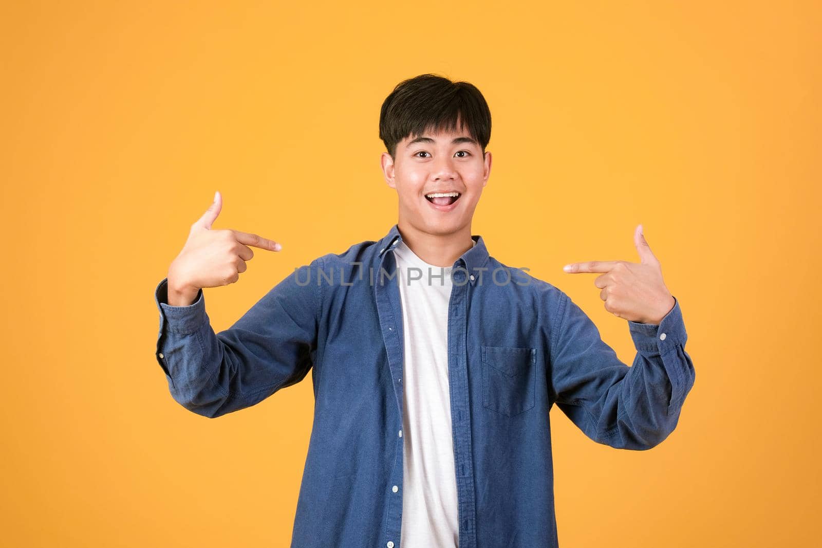 Choose An Pick Me. Confident young man pointing and promoting himself. Portrait asia young man isolated over yellow  orange studio background.