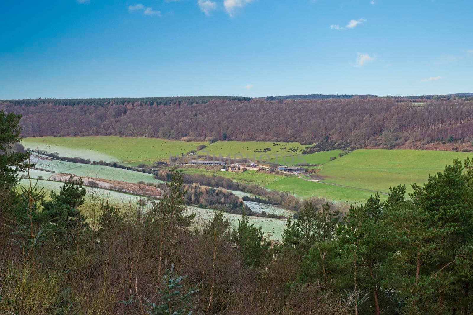 Panoramic view over rural countryside farming landscape with fields in a valley during winter frost