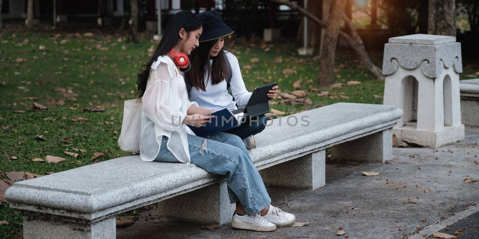 Asian woman traveler with backpack using maps on tablet and sitting in park, travel holiday relaxation concept