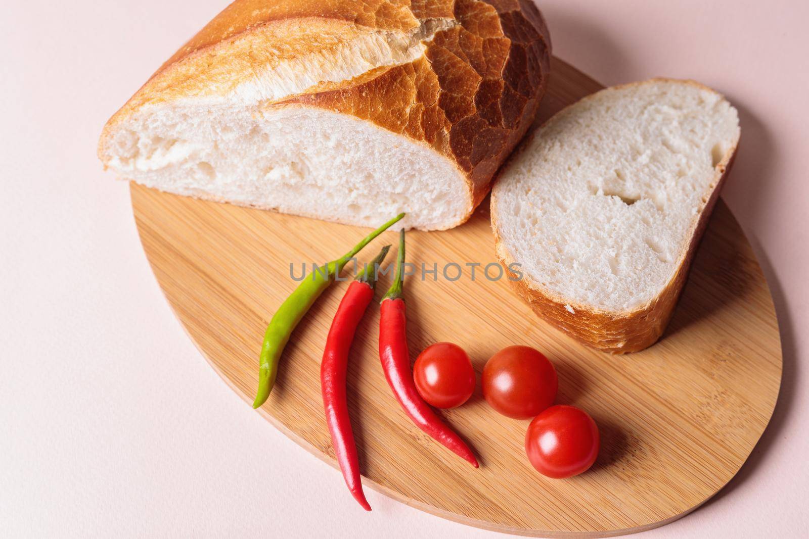 Sliced pieces of white bread with red peppers and tomatoes on a cutting board. Light background