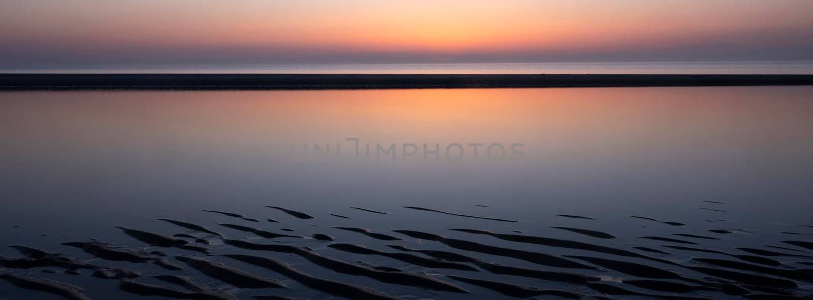 pattern in sand and colorful reflection of setting sun in water by ahavelaar