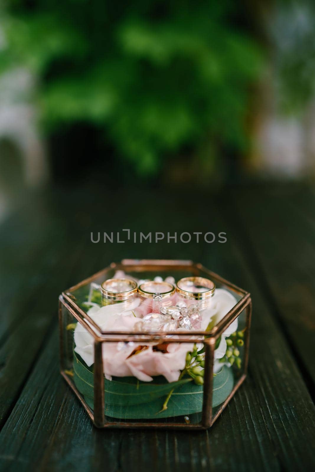 Wedding rings of the bride and groom and the engagement ring on a decorative glass box with a pink flower inside. High quality photo