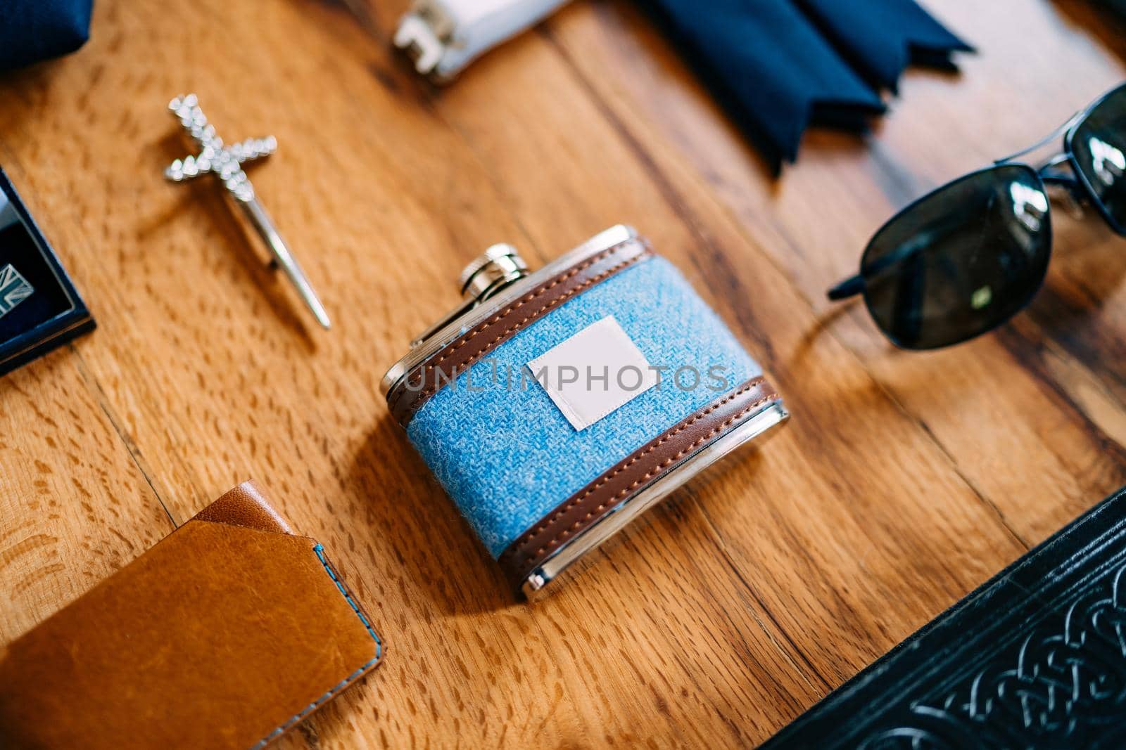 Close-up of a male blue jar with brown leather inserts with a purse, sunglasses and a cross on a smooth wooden surface. High quality photo