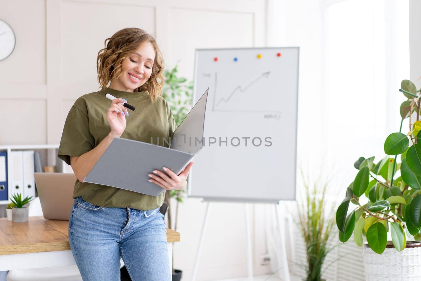 Businesswoman holding folder for paper write marker thinking dreaming standing near office table. Business person femal ypoung adult caucasian on modern white interior