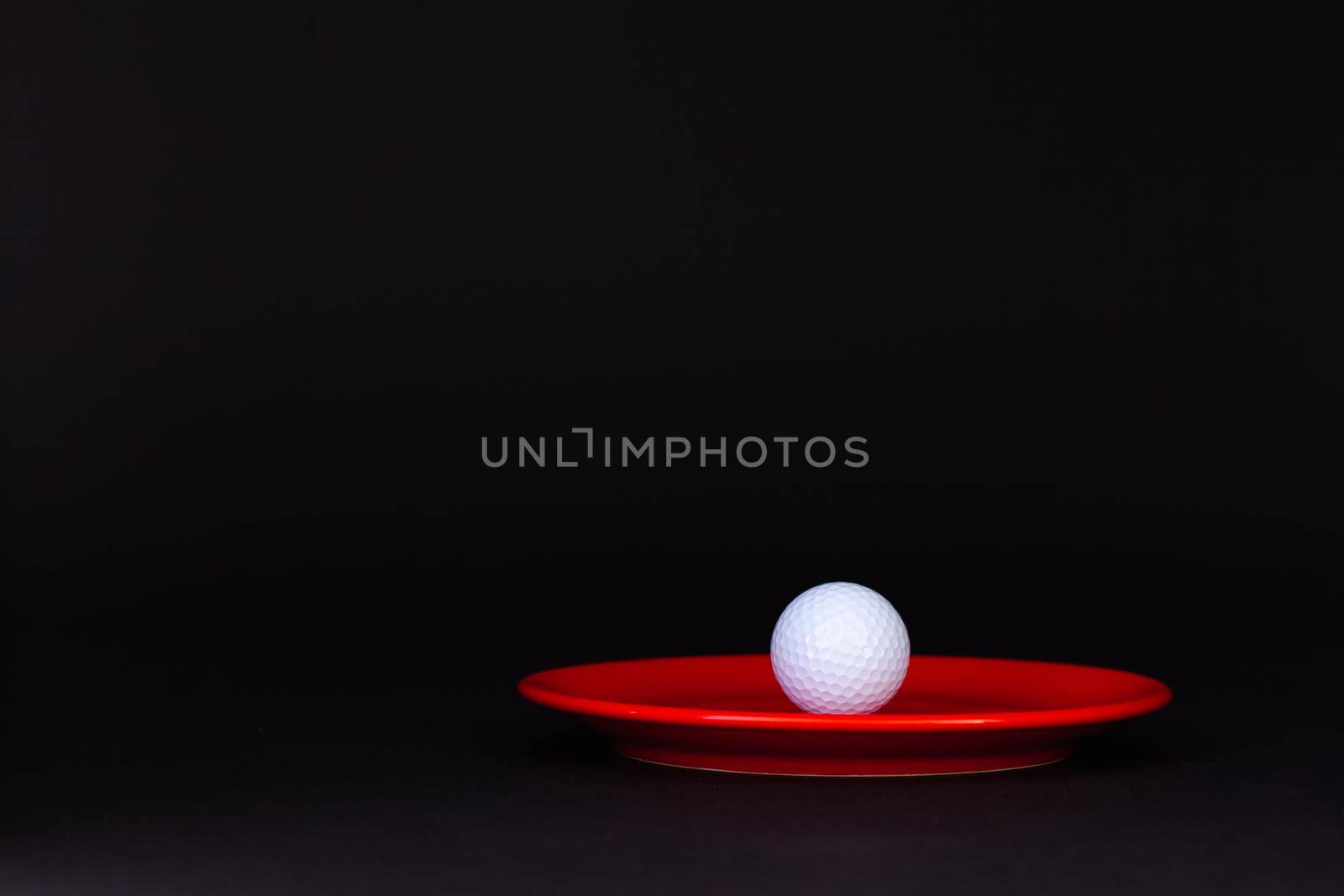 Red plate and golf ball on the black background