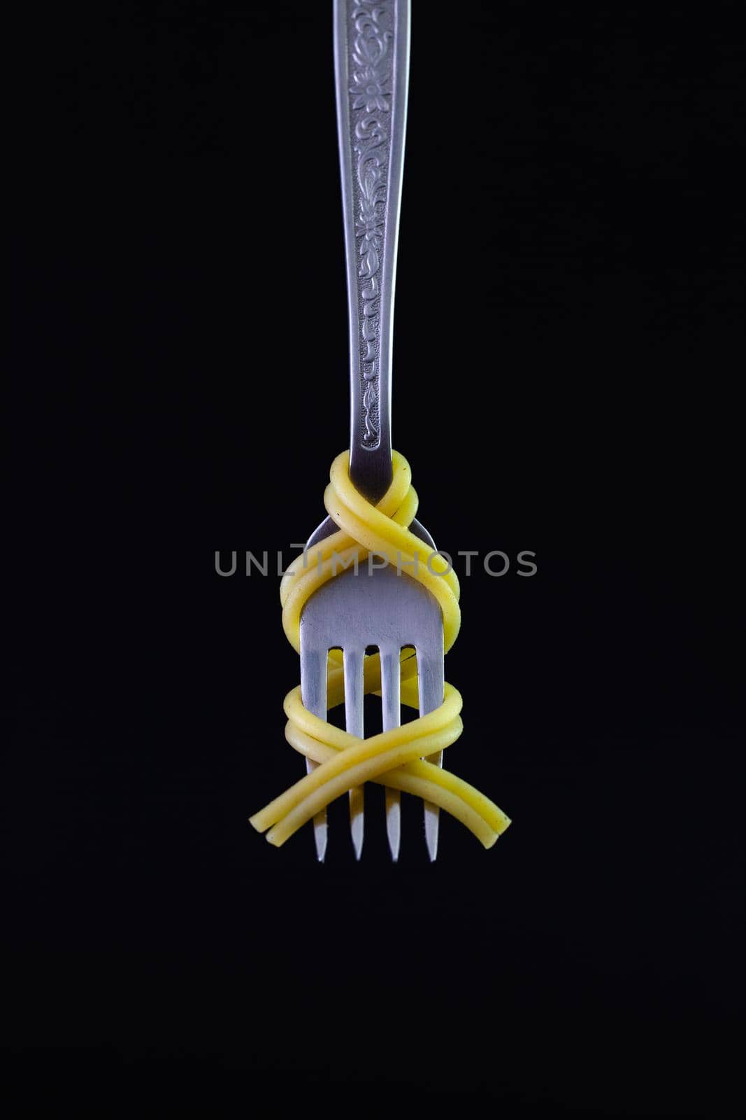 Freshly cooked pasta on a old fork on the black background. Symmetrical loop of spaghetti on an old fork.