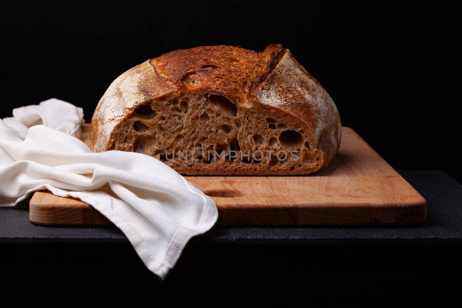 Artisan sourdough bread. Freshly baked round loaf of sourdough bread with linen cloth on black background