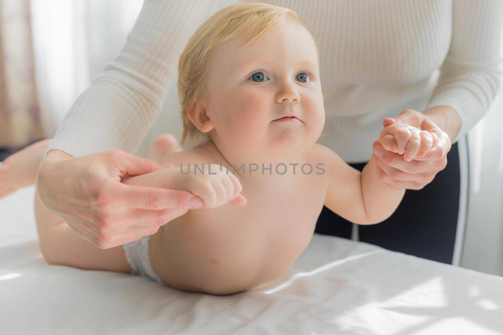 Mom does hand exercises to the baby. Close-up. A satisfied baby lies on the massage table on his stomach.