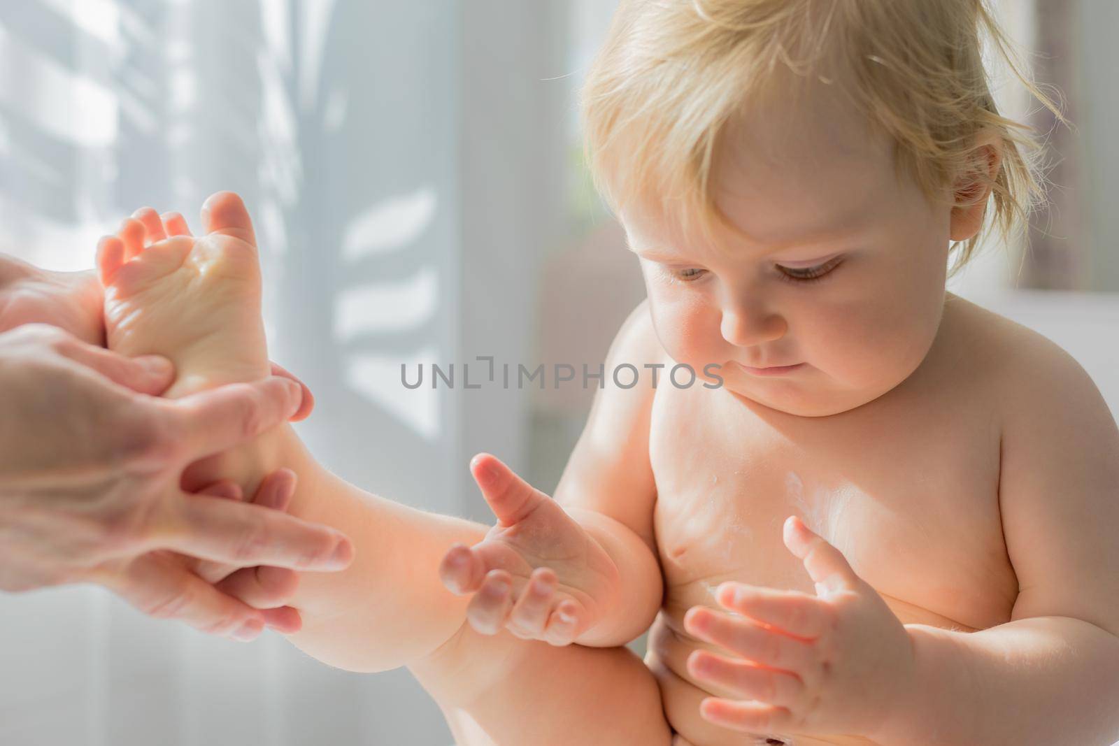 Mom gives her baby a leg and foot massage. Close-up. A satisfied baby is sitting on a massage table.