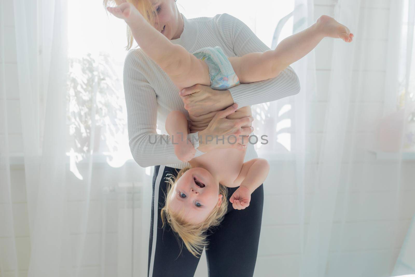 Mom holds the baby upside down, is engaged in children's gymnastics. Both are happy and laughing.