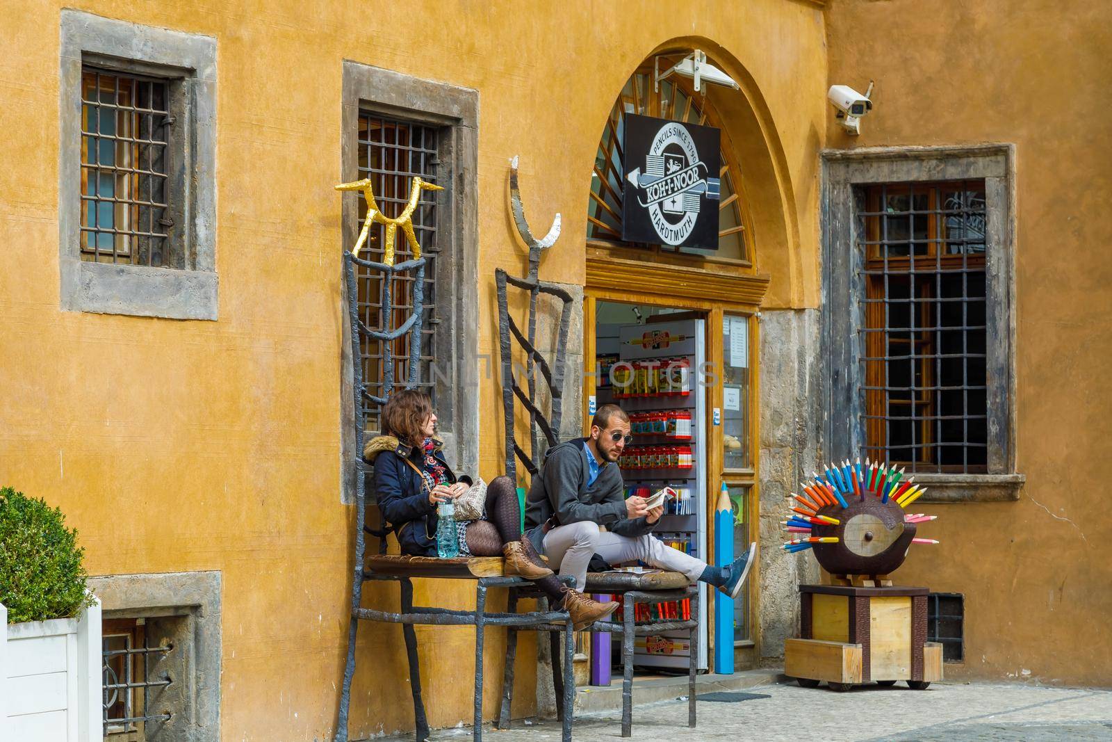A girl and a guy are sitting on large chairs at the entrance to the pencil store. Prague, Czech Republic April 14, 2018