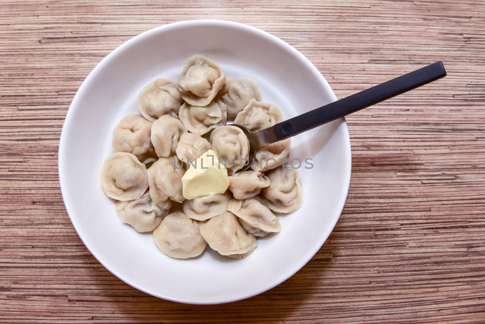 plate with homemade Russian dumplings on a wooden table and a spoon next to it.